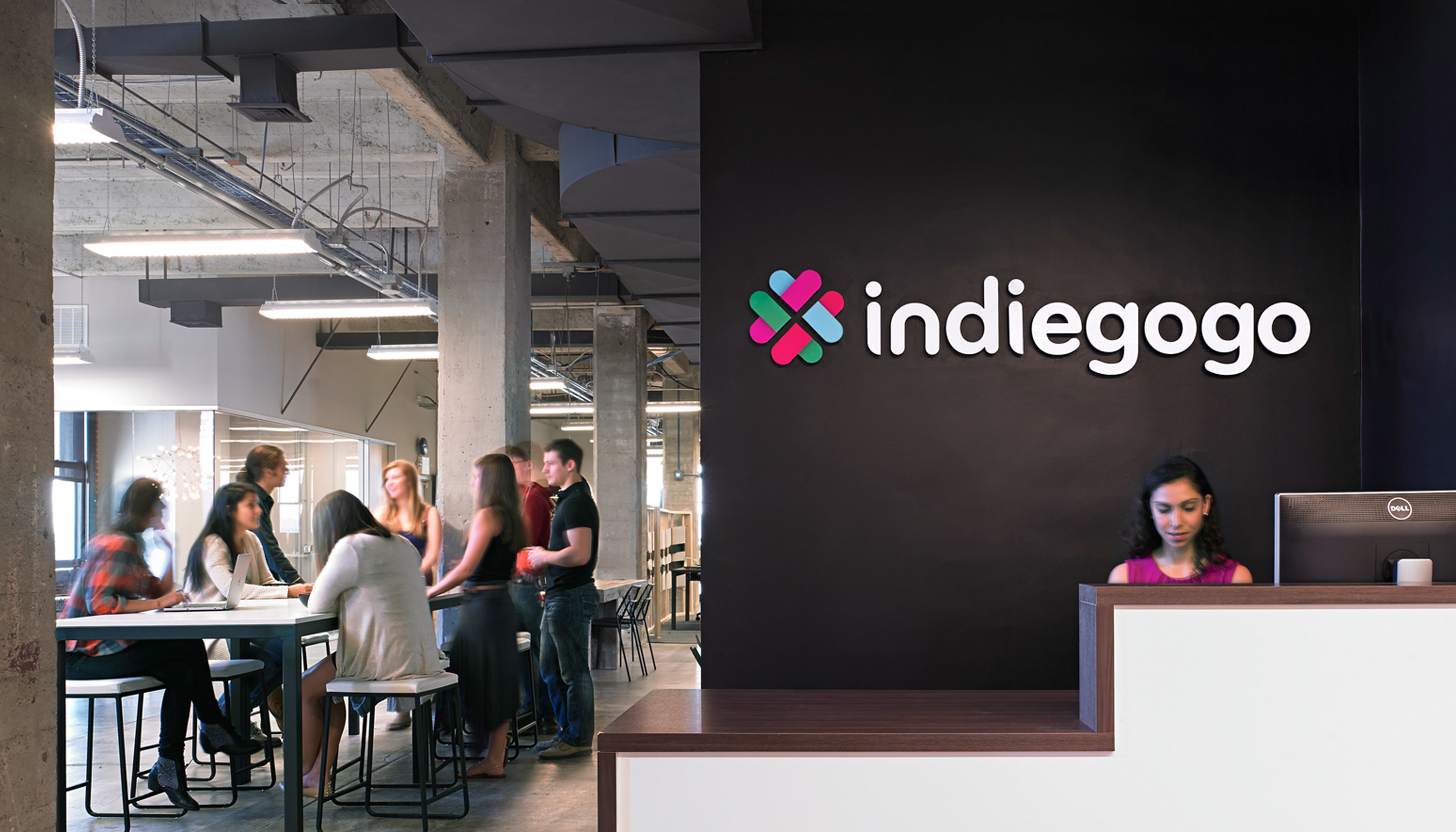 indiegogo offices reception desk with people working at table and logo signage on wall
