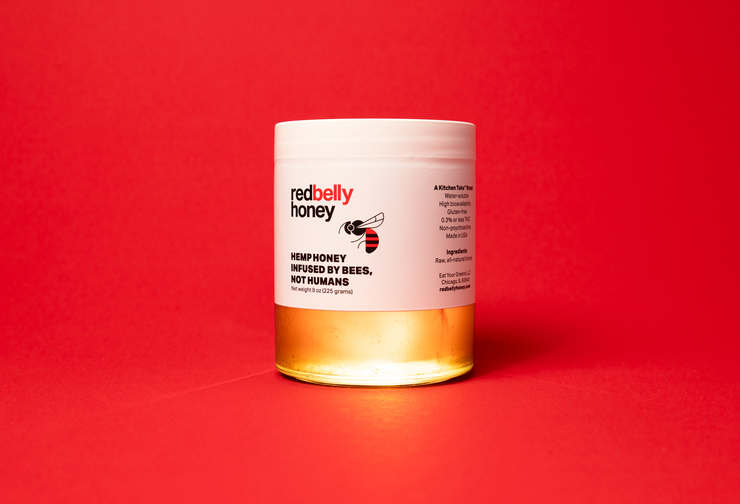 jar of red belly honey with light shining through glass on red backdrop