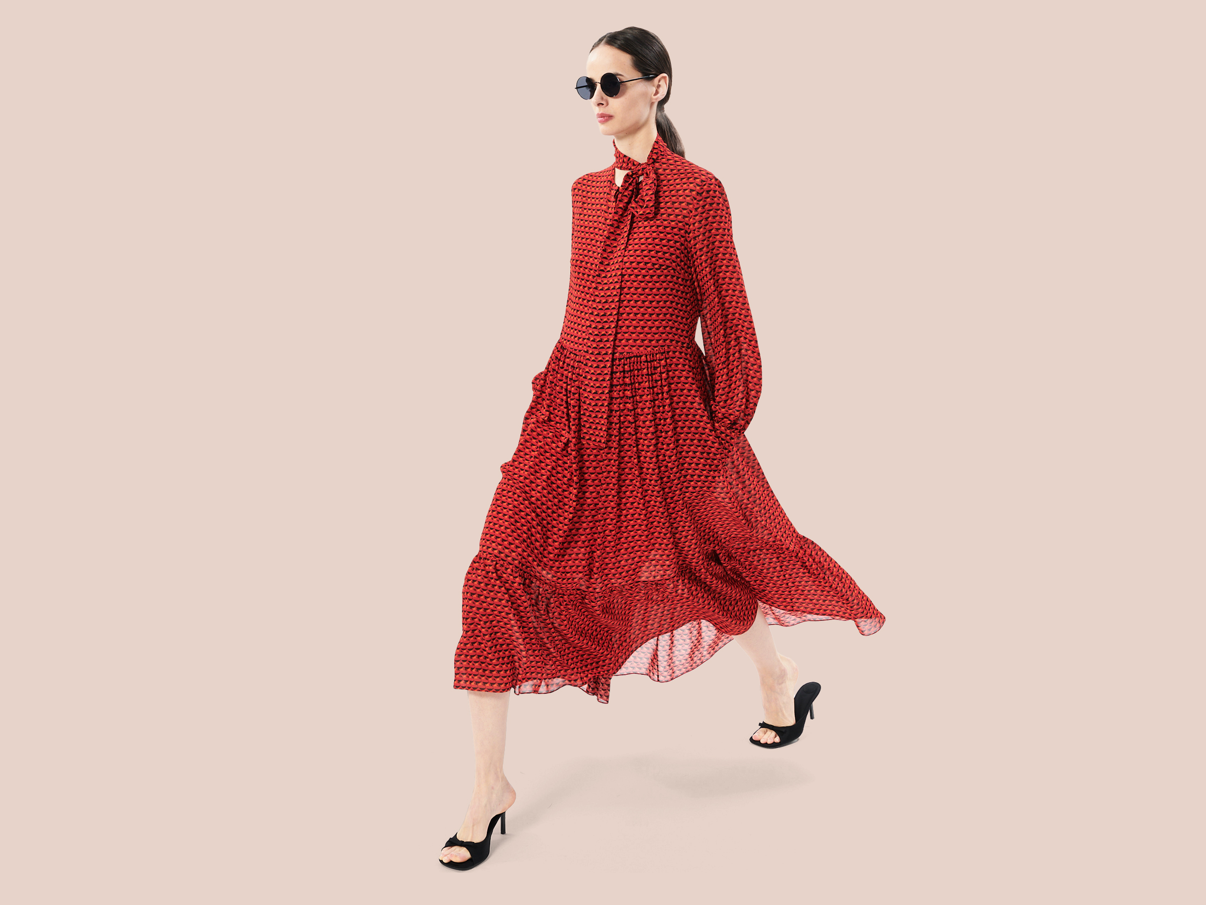 brunette model wearing a red dress and black heels with orange and black bird pattern